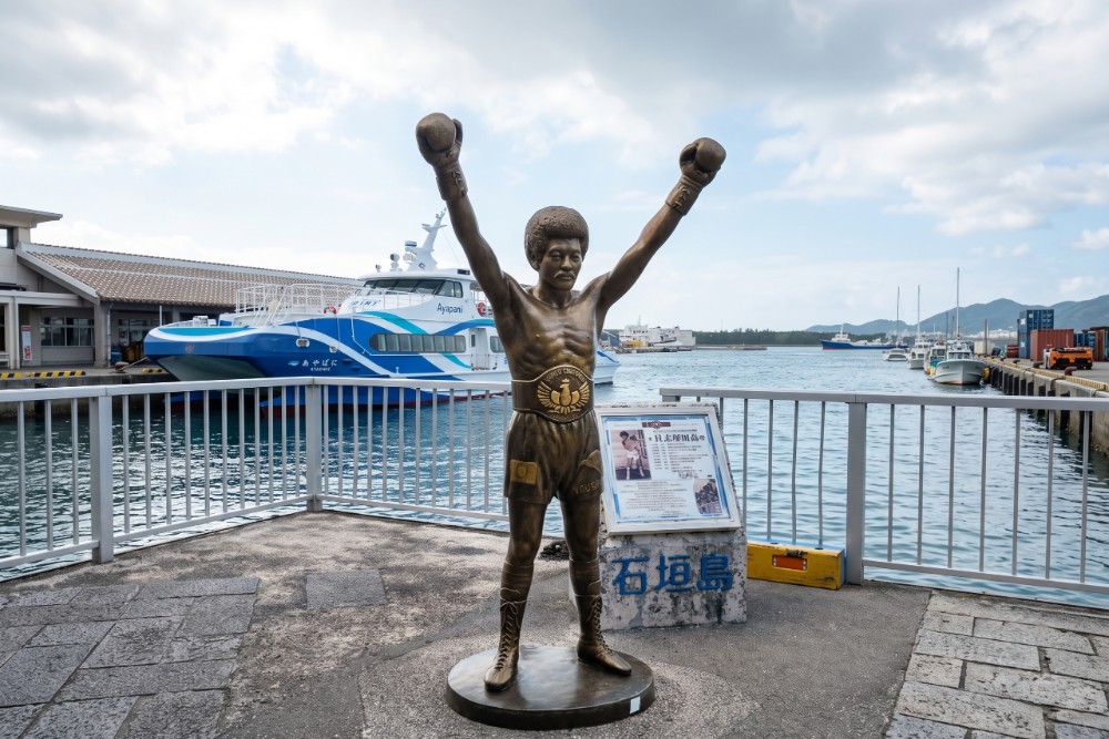 離島碼頭前方，豎立著一座金光閃閃的拳擊手銅像，他是石垣島出身的傳奇英雄——前WBA輕蠅量級世界冠軍「具志堅用高」。